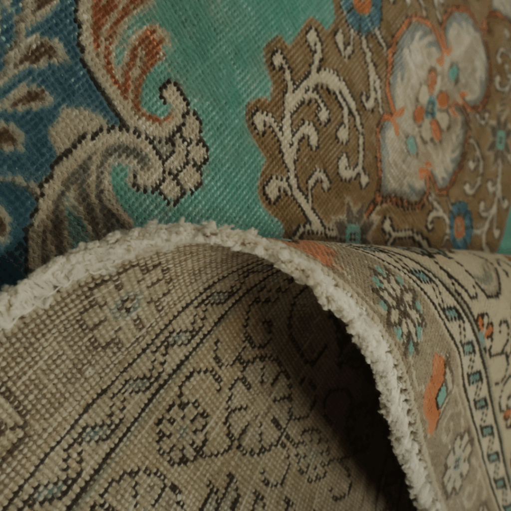 Another close-up of the same ornate rug with teal, tan, and beige designs, showing its thickness and detailed floral motifs.