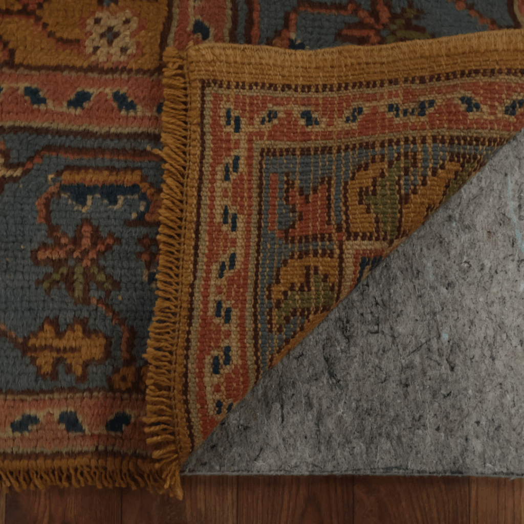 Another close-up of the same traditional rug, showing its detailed woven border in warm orange, gold, and blue tones against a gray field.