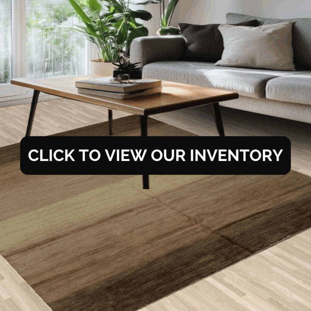 A cozy living room with a gray sofa, wooden coffee table, and green plants by a bright window. A neutral brown area rug grounds the space, with text across the center reading, “Click to view our inventory.