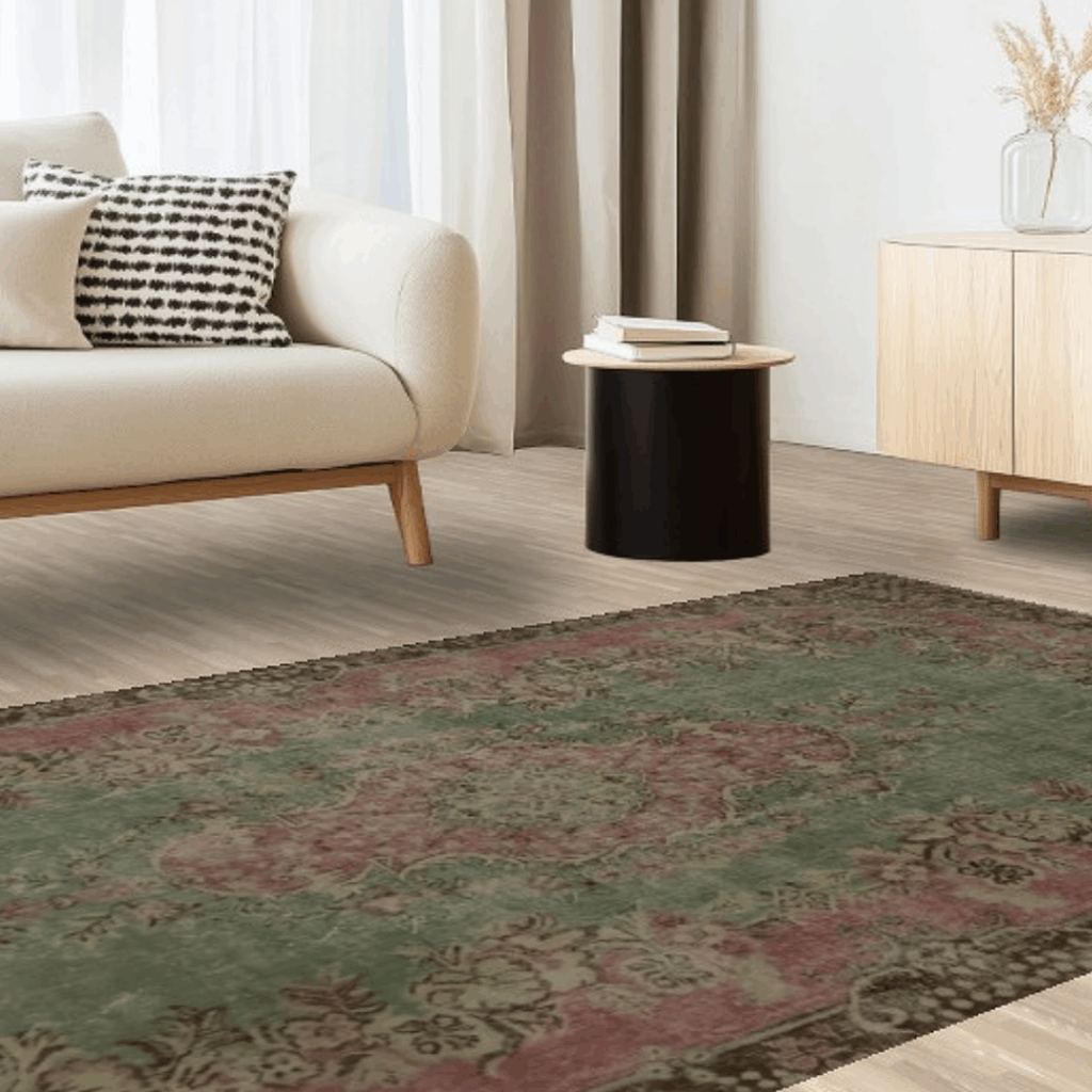 A cozy minimalist room with a cream sofa, small black side table, and light wood furniture. A faded green and red patterned rug anchors the scene, adding warmth to the neutral space.