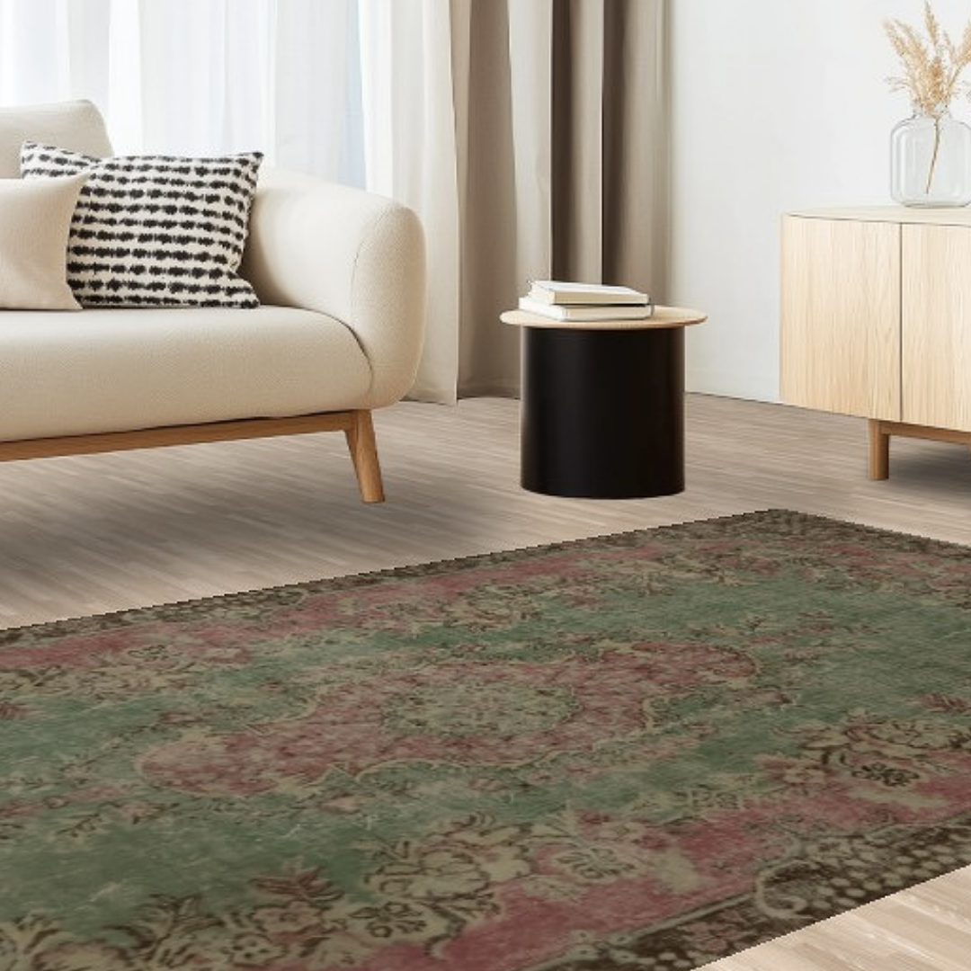 A cozy minimalist room with a cream sofa, small black side table, and light wood furniture. A faded green and red patterned rug anchors the scene, adding warmth to the neutral space.