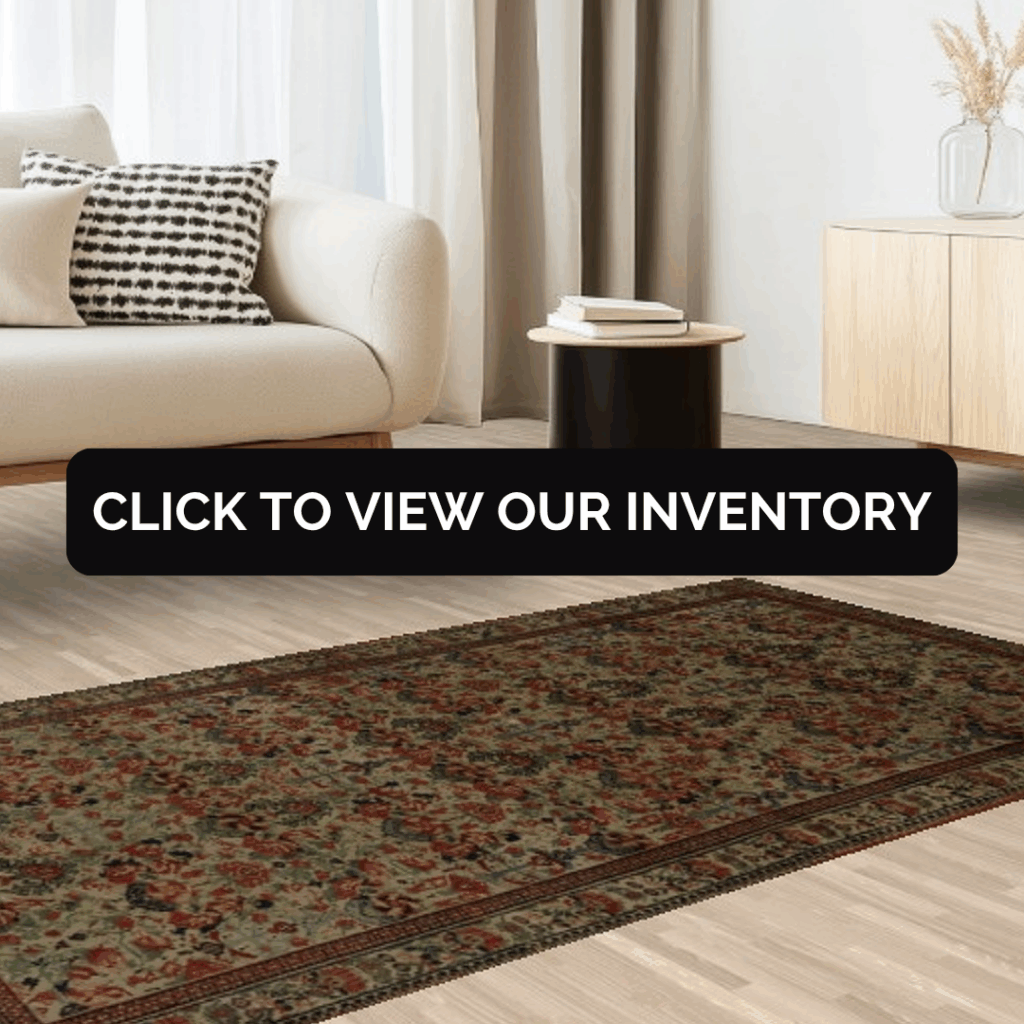 A minimalist living space with a beige sofa, patterned pillow, and a rectangular floral rug in rich green and red hues on light wood flooring. A black side table and light wood cabinet complete the decor.