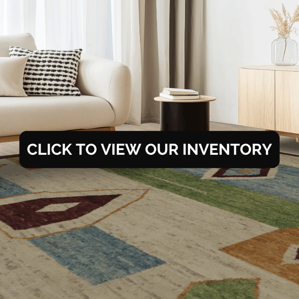 A modern, cozy living space featuring a cream-colored sofa with a black-and-white patterned pillow beside a small round side table. A colorful rug with geometric shapes in green, blue, and rust tones adds warmth to the neutral room. Text overlay reads “Click to View Our Inventory.”