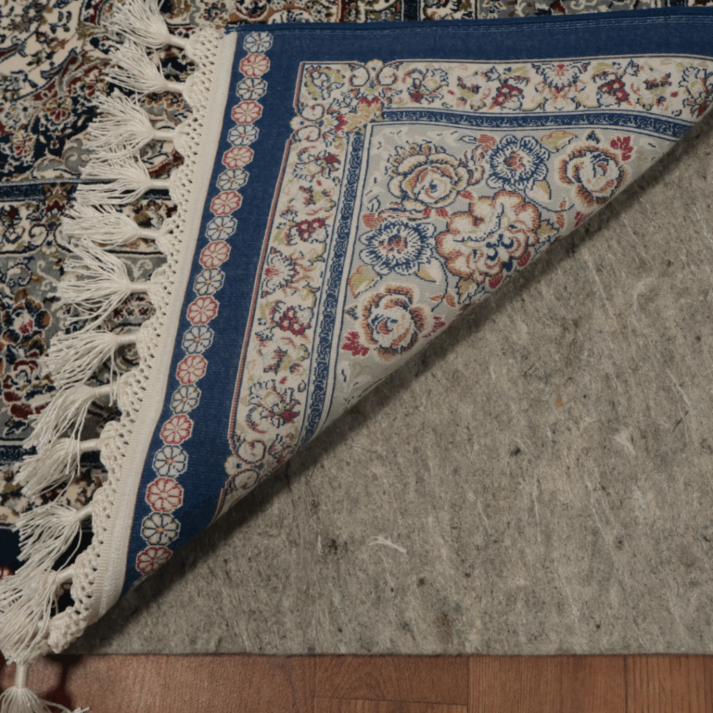 A corner view of a woven rug with floral patterns in blue, cream, and red tones, partially flipped to reveal the underside and fringed edge.